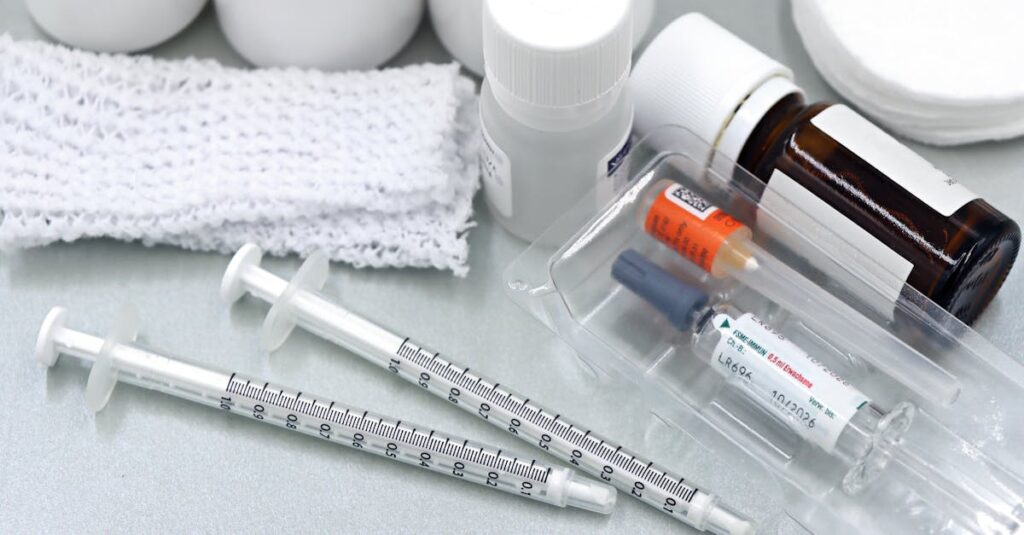 Flat lay of medical tools and vaccines, including syringes and bottles, on a white surface.